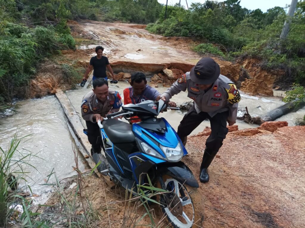 Anggota polisi membantu masyarakat menyeberangi jalan yang putus sebelum diperbaiki, foto beberapa hari lalu. (ft wandy)