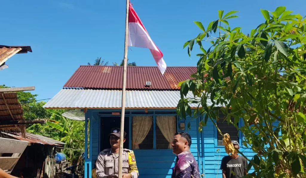 Kades dibantu Bhabinkamtibas Desa Tanjung Harapan melakukan pemasangan bendera merah putih untuk warga, pagi tadi. (ft fuji)